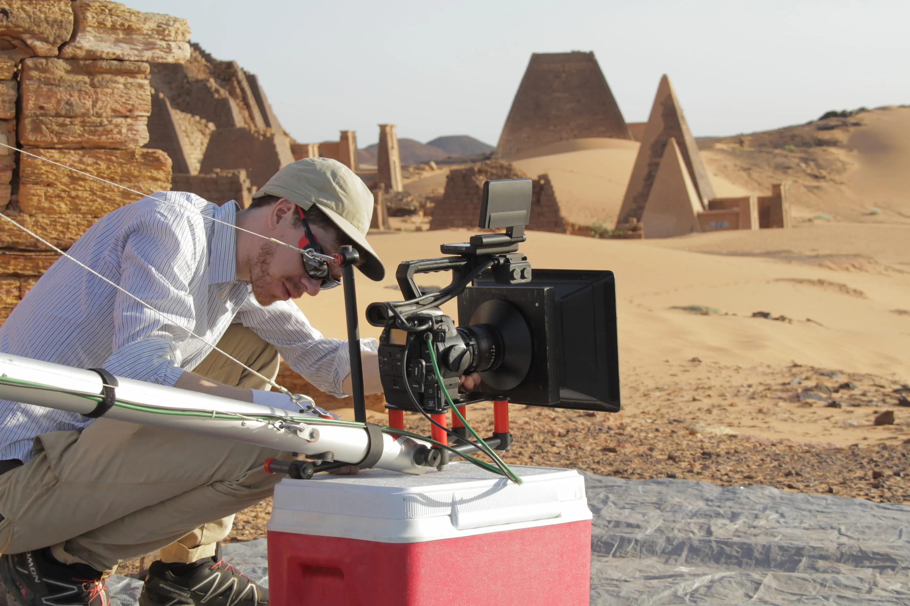 Kameramann hinter einer auf einem Kran montierten Kamera. Im Hintergrund Pyramiden.