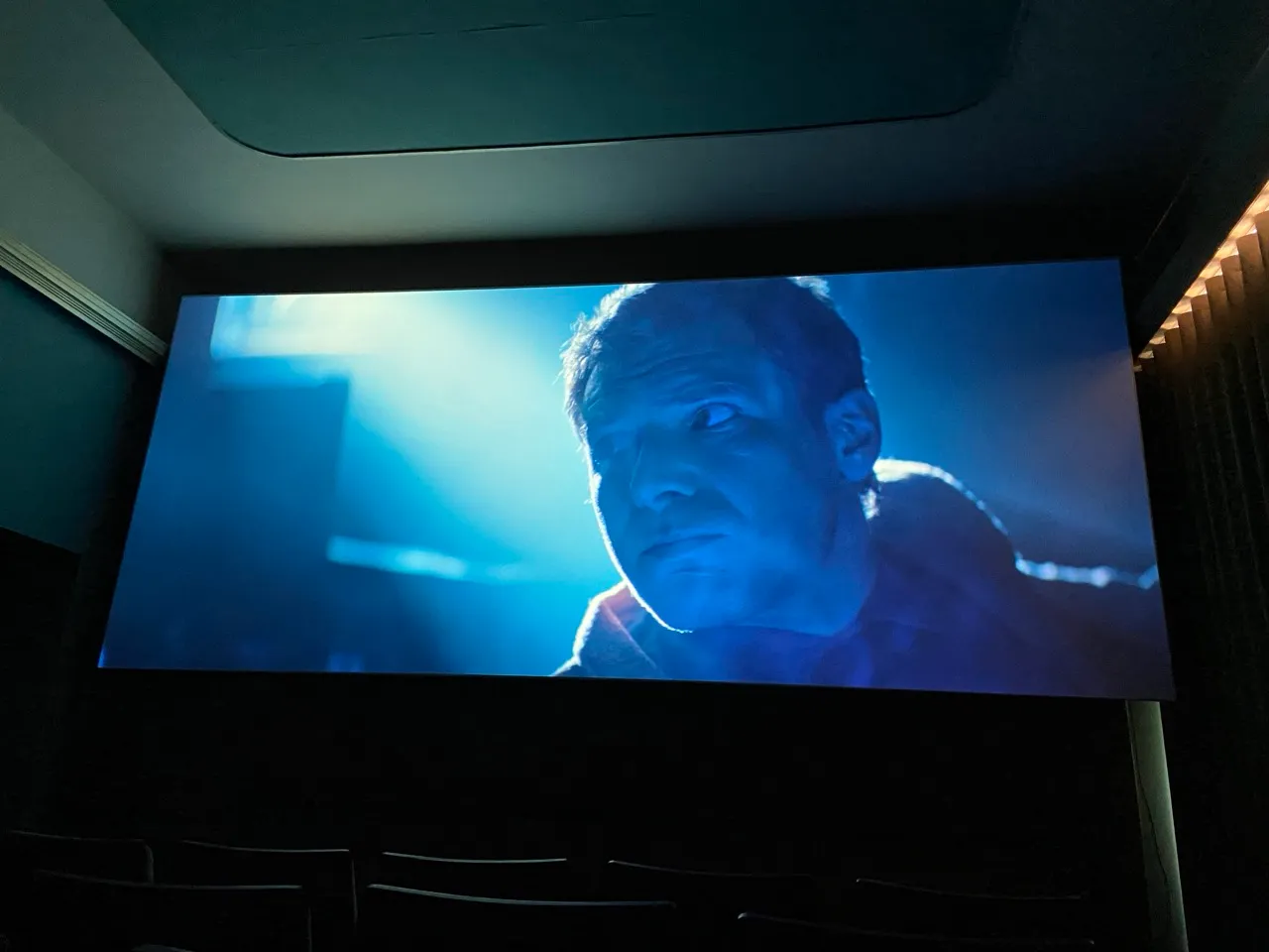 Inside a dark lit cinema. On the screen a close up of an actors face all lit up in blue.